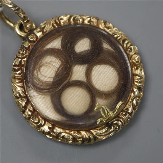 An early 19th century yellow metal mounted circular mourning pendant, with hair beneath glazed panel, 23mm.